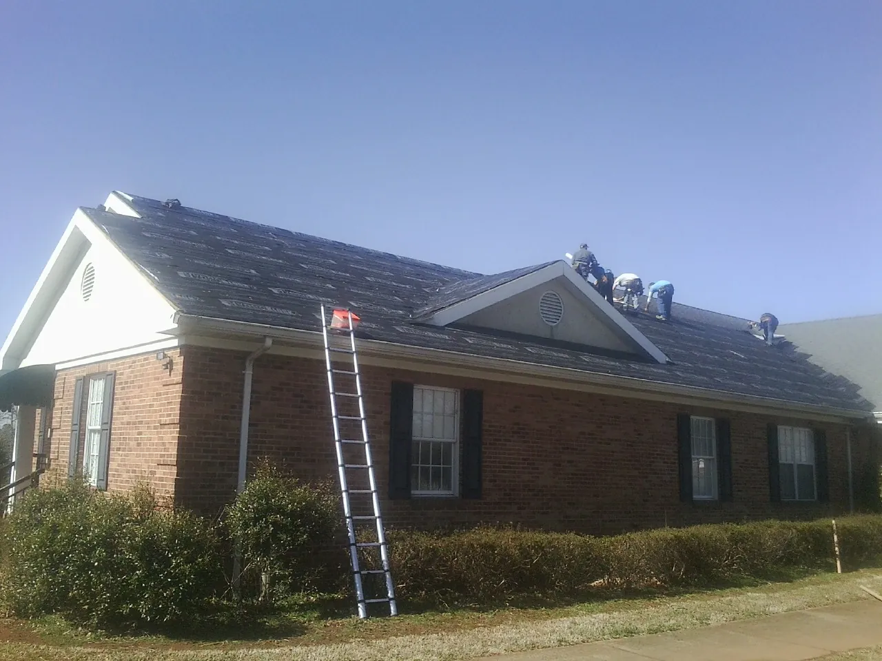 Crew tearing shingles off a brick ranch roof with a ladder set — Emergency Roof Repair work by our crew in Langhorne