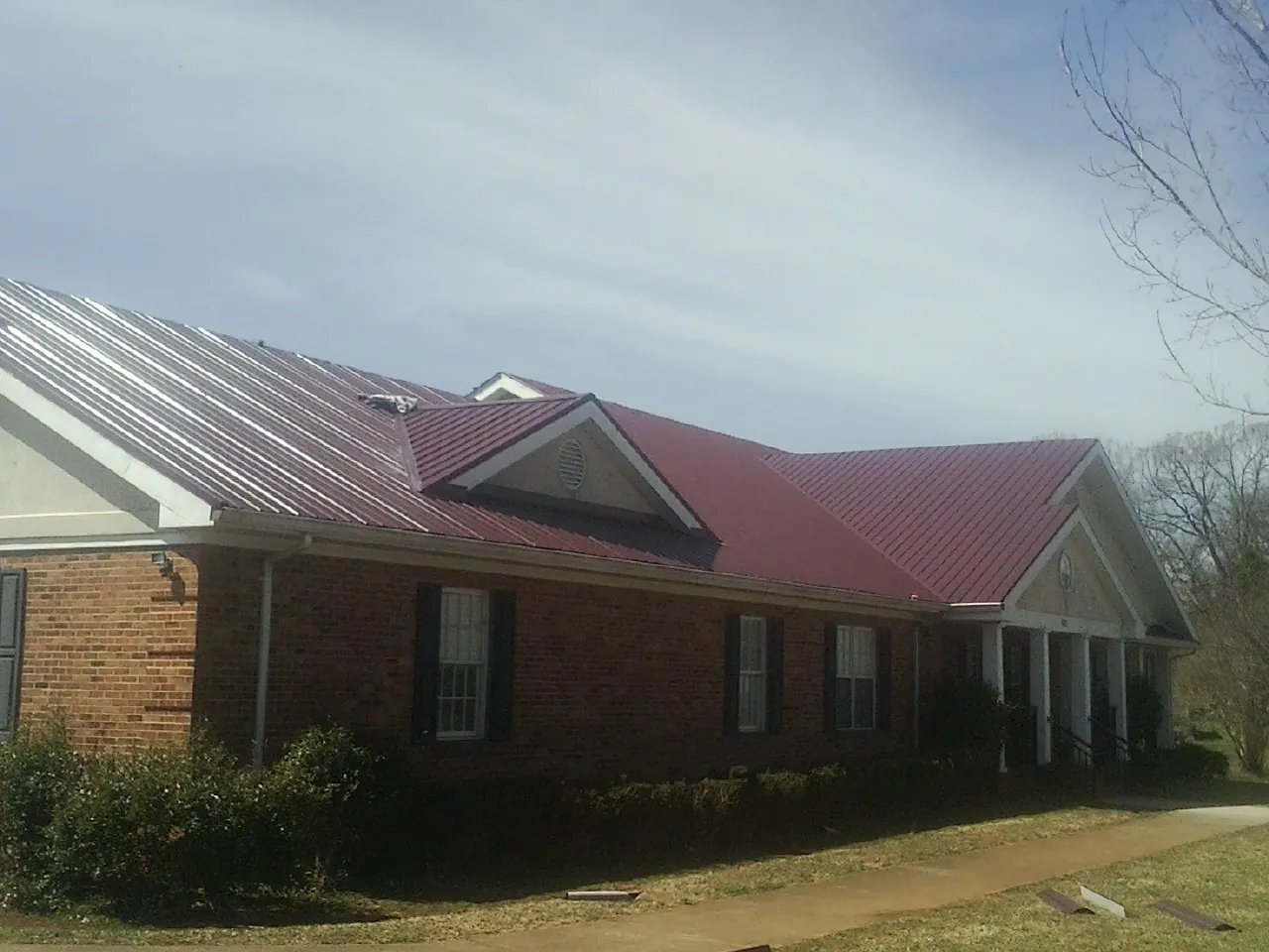 Red metal roof with gabled entries on a long brick building, from a Hail Damage Roof Repair job in Langhorne