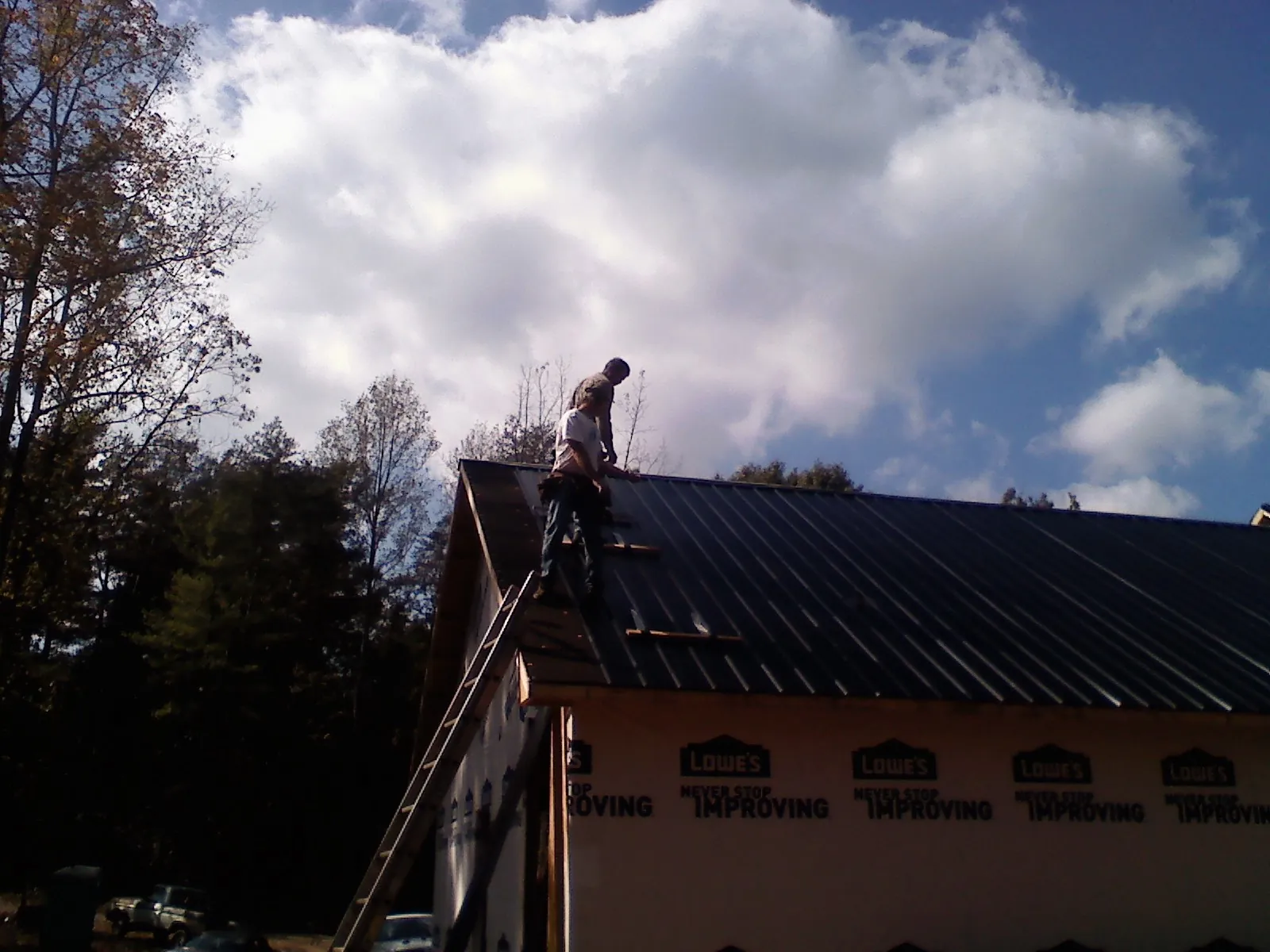 Roofer fastening dark metal panels high against a cloudy sky, from a Roof Inspection job in Langhorne