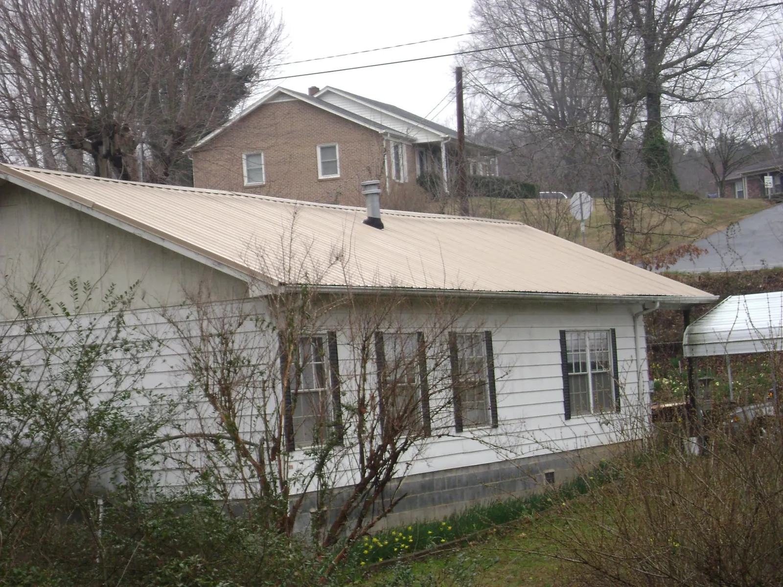 Tan metal roof on a white sided house set into a hillside — Commercial Roofing by Roofing Brothers in Langhorne